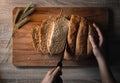 Woman hands cutting home made and baked grain bread on a wooden table with floral decoration Royalty Free Stock Photo