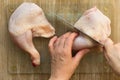 Woman hands cutting raw chicken leg in two part with knife raw on glass cutting board on wooden background Royalty Free Stock Photo