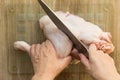 Woman hands cutting raw chicken leg in two part with knife raw on glass cutting board on wooden background Royalty Free Stock Photo