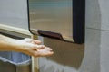 Woman hands dries wet hand in modern vertical hand dryer in public restroom