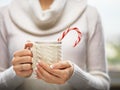 Woman hands with elegant french manicure nails design holding a cozy knitted mug with cocoa and a candy cane. Royalty Free Stock Photo