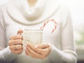 Woman hands with elegant french manicure nails design holding a cozy knitted mug with cocoa and a candy cane. Royalty Free Stock Photo