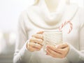 Woman hands with elegant french manicure nails design holding a cozy knitted mug with cocoa and a candy cane. Royalty Free Stock Photo