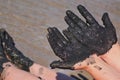 Woman hands and feet covered with black healing mud, sandy seashore in background