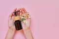 Woman hands, flowers and glass bottle with cosmetic product on pink background