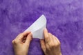 Woman hands folding paper triangle to make smaller triangle on the violet surface