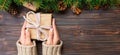 Woman hands give wrapped christmas handmade present in paper with pink ribbon. Present box on holiday on dark wooden table, banner