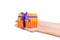 Woman hands give wrapped Christmas or other holiday handmade present in orange paper with purple ribbon. Isolated on white Royalty Free Stock Photo