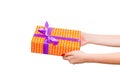 Woman hands give wrapped Christmas or other holiday handmade present in orange paper with purple ribbon. Isolated on white Royalty Free Stock Photo