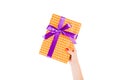 Woman hands give wrapped Christmas or other holiday handmade present in orange paper with purple ribbon. Isolated on white Royalty Free Stock Photo