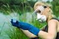 Woman with hands in gloves holds a glass with a sample of water. Sampling from open water Royalty Free Stock Photo