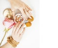 woman hands with golden manicure and many rings holding brushes, flower, makeup stuff on white background copyspace