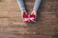Woman hands in gray sweater on wood table giving red Christmas gift box wrapped with white ribbon Royalty Free Stock Photo