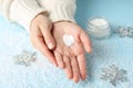 Woman hands, heart shape created from winter cream, jar of winter cream for skin on snowy blue background