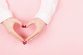 Woman hands in a heart shape on pink background.