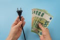 Woman hands hold electric plug and euro banknotes over blue background. High energy costs in Europe. Electric bill increases Royalty Free Stock Photo