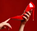 Woman hands hold red high hill shoe on dark red