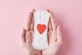 Woman hands hold sanitary pad with red heart on a pink background Royalty Free Stock Photo