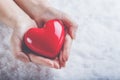 Woman hands are holding a beautiful glossy red heart in a snow background. Love and St. Valentine concept.