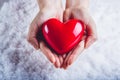 Woman hands are holding a beautiful glossy red heart in a snow background. Love and St. Valentine concept.