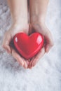 Woman hands are holding a beautiful glossy red heart in a snow background. Love and St. Valentine concept. Royalty Free Stock Photo