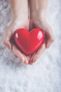 Woman hands are holding a beautiful glossy red heart in a snow background. Love and St. Valentine concept. Royalty Free Stock Photo