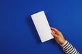 Woman hands holding blank white flyer brochure booklet. Mockup sheet template advertising booklet on blue background