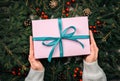 Female hands in pullover holding Christmas gift box decorated with evergreen fir branch background. Christmas and New Year. top Royalty Free Stock Photo