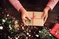 A woman hands holding a Christmas gift with a red ribbon and snow over on a wooden table. Royalty Free Stock Photo