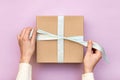 Woman hands holding craft gift box with blue bow on pastel pink background. Girl binds classic bow for present box. Top view, flat Royalty Free Stock Photo