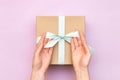 Woman hands holding craft gift box with blue bow on pastel pink background. Girl binds classic bow for present box. Top view, flat Royalty Free Stock Photo