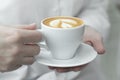 Woman hands holding cup of hot coffee latte cappuccino with with lush milk foam heart shaped. Royalty Free Stock Photo