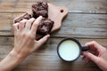 Woman hands holding a cup of milk and taking a chocolate cake with cherries. Eating at home concept. Royalty Free Stock Photo