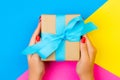 woman hands holding gift wrapped and decorated with blue bow on blue, pink and yellow background with copy space Royalty Free Stock Photo