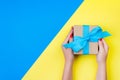 Woman hands holding gift wrapped and decorated with blue bow on blue and yellow background with copy space Royalty Free Stock Photo