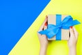 woman hands holding gift wrapped and decorated with blue bow on blue and yellow background with copy space Royalty Free Stock Photo