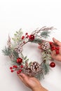 Woman hands are holding handmade reusable Christmas wreath made of tree branches, red berries, cones on white backdrop Royalty Free Stock Photo