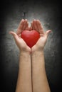 Woman hands holding heart over a dark concrete wall