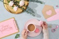 Woman hands holding macaroon and coffee cup with flowers and card on light blue background. Top view, flatlay Royalty Free Stock Photo