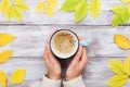 Woman hands holding morning cup of coffee on vintage wooden table decorated autumn yellow leaves top view. Cozy fall breakfast.