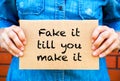 Woman hands holding piece of cardboard with phrase Fake It Till