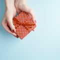 Woman hands holding red gift with ribbon, manicured hands with nail polish on aquamarine background with copy space