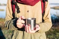 Woman hands holding a steaming cup of in beautiful nature environment. Enjoying a coffee in tourist metal cup at a hiking trip Royalty Free Stock Photo