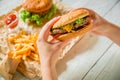 Woman hands holding tasty american burger and french fries, sauce on wooden plate Royalty Free Stock Photo