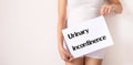 Woman hands holding a white sign with the word urinary incontinence on white background