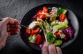 Woman hands with knife and fork eat Fresh salad with chicken breast, cheese, black olives,red pepper, lettuce, fresh sald leaves a Royalty Free Stock Photo