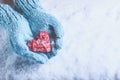 Woman hands in light teal knitted mittens are holding beautiful entwined vintage red heart on snow. Love, St. Valentine concept. Royalty Free Stock Photo
