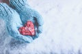 Woman hands in light teal knitted mittens are holding beautiful entwined vintage red heart on snow. Love, St. Valentine concept.