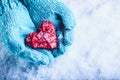 Woman hands in light teal knitted mittens are holding beautiful entwined vintage red heart in a snow. St. Valentine concept.