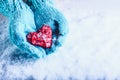 Woman hands in light teal knitted mittens are holding beautiful entwined vintage red heart in a snow. St. Valentine concept. Royalty Free Stock Photo